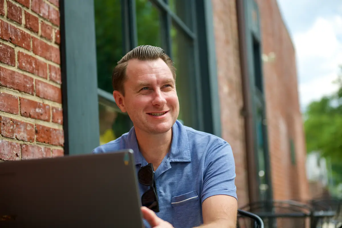 Lee Procida smiling while working on a laptop at a sidewalk café in Haddonfield